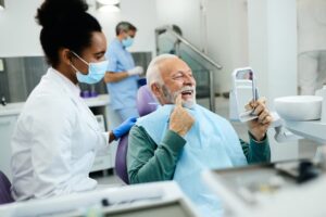 Dental hygienist watches as patient examines teeth using a mirror at the dentist’s office