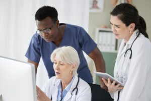 Three healthcare providers reviewing electronic medical records on computer screen